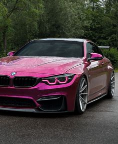 a pink bmw is parked on the side of the road in front of some trees