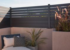 an outdoor seating area with pillows and plants on the side of the wall, next to a fence