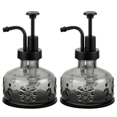 two glass soap dispensers with black handles and flowers on the front one is clear