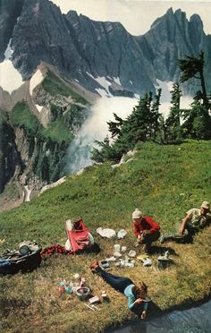 several people are camping in the mountains with backpacks and food on the grass near water