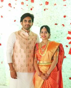 a man and woman standing next to each other in front of a wall with flowers