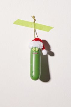 a green pickle with a santa hat hanging from it's side on a string