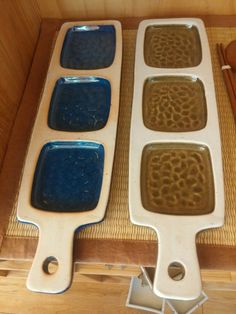 two pans with blue and brown food in them on a wooden table next to utensils