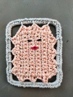 a crocheted square with a face on the front and bottom, in light pink