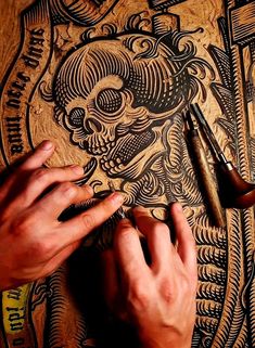 two hands are working on an intricately designed piece of art with scissors and ink