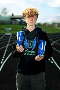 a young man standing on top of a race track holding a pair of shoes in his hands