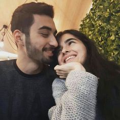 a man and woman smile at each other while they pose for a photo in front of some greenery