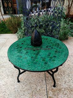 a green table sitting on top of a tiled floor next to a planter filled with flowers