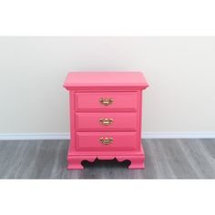 a pink chest of drawers with gold handles and knobs on the bottom, against a white wall