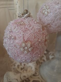 two pink ornaments are hanging on a lace doily