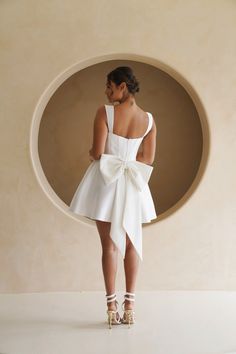 a woman standing in front of a circular wall wearing high heels and a white dress