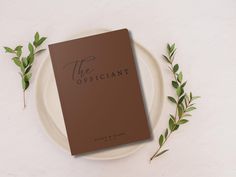 the officialant book on a plate next to some green leaves and twig sprigs