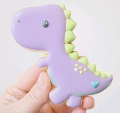 a hand holding a purple dinosaur toy with green and yellow decorations on it's body