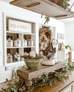 a wooden table topped with a bowl filled with greenery next to a christmas tree