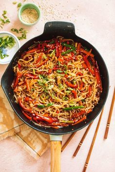 a pan filled with noodles and vegetables next to chopsticks