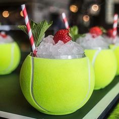 three tennis balls with strawberries and mint garnish in them on a table