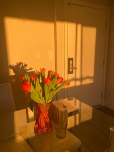 a vase filled with red flowers sitting on top of a table next to a chair