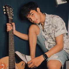 a young man sitting on top of a chair holding a guitar