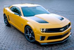 a yellow chevrolet camaro is parked on a cobblestone street in front of a building