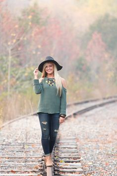 a woman wearing a black hat and green sweater posing on train tracks with her hand up in the air