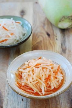 two bowls filled with food sitting on top of a wooden table next to an onion and cabbage salad