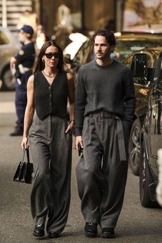 a man and woman are walking down the street with cars in the backgrouds