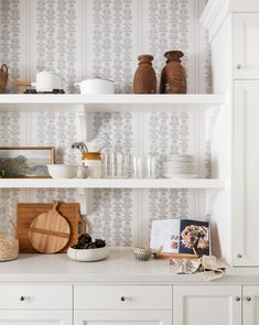 a kitchen with white cupboards and shelves filled with plates, bowls and utensils