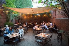 an outdoor dining area with people sitting at tables and lights strung from the ceiling over them