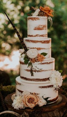 a three tiered cake with white flowers and gold glitters on top is sitting on a tree stump