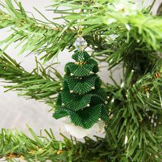 a green christmas tree ornament hanging from a pine branch with beads on it