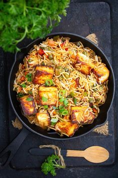 a pan filled with rice and tofu on top of a black tray next to some parsley