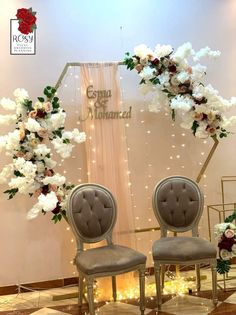 two chairs sitting in front of a floral arch with white flowers on the back ground