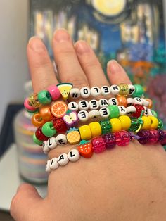 a person's hand holding several bracelets with letters and fruit charms on them