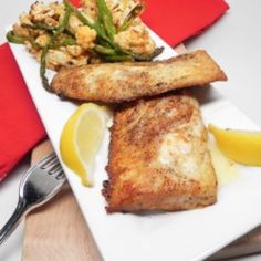 fish, asparagus and lemon wedges on a white plate with red napkin