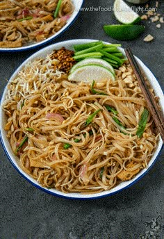 two white plates filled with noodles and vegetables next to chopsticks on a table