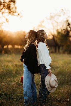 two women are standing in the grass and one is holding a cowboy's hat