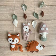 three felt animals hanging from strings on a wooden surface with leaves and mushrooms in the background