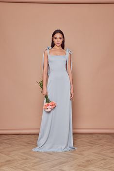 a woman in a long blue dress holding a bouquet and standing on a wooden floor