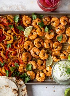 a tray filled with shrimp and vegetables next to tortillas