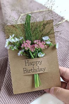 a person holding a card with flowers on it that says happy birthday in front of them