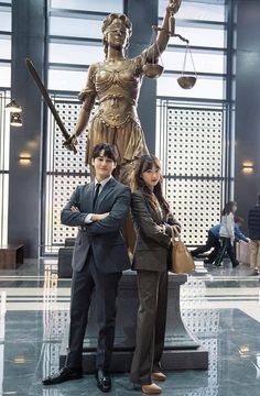 two people standing next to each other in front of a statue with scales on it