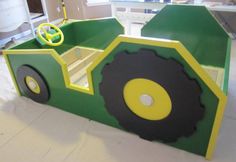 a green and yellow tractor shaped bed with wheels on the bottom, sitting in a room