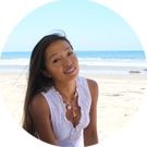 a young woman standing on top of a sandy beach next to the ocean with her hands in her pockets