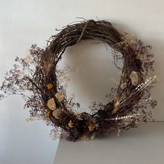 a wreath made out of branches and dried flowers on a white surface with no one around it