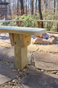 a wooden bench sitting on top of a stone floor next to trees and rocks in front of a fire pit