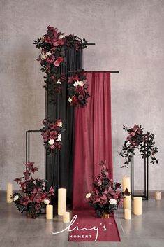 an arrangement of flowers and candles is displayed on the floor next to a red curtain