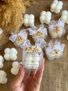 a hand holding a small jar filled with marshmallows on top of a table