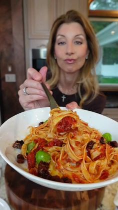 a woman holding a fork in a bowl of pasta