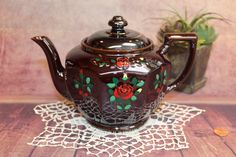 a teapot with flowers painted on it sits on a doily next to a potted plant