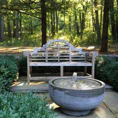 an outdoor fountain in the middle of a park with a bench and trees behind it